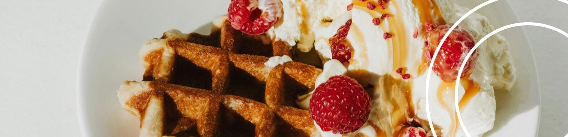 A breakfast waffle with 2 scoops of vanilla ice cream, fresh raspberries and a toffee sauce topping